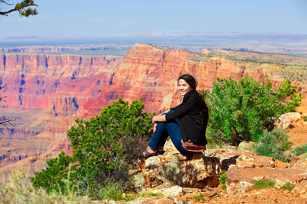 Biracial teen girl sitting along rock ledge at Grand Canyon stock photo