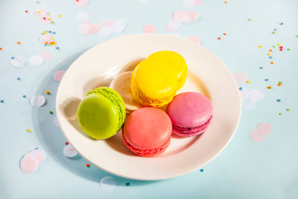 Birthday party concept. Colorful macaroons on the white plate, Glasses and wine bottle on the background. stock photo