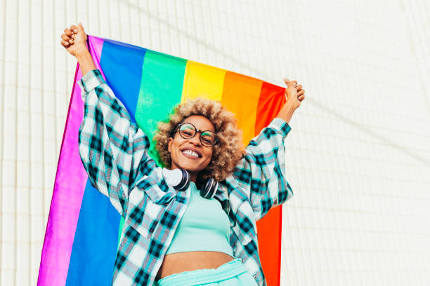 Black afro woman holds up lgbtq flag of gay pride outdoors stock photo