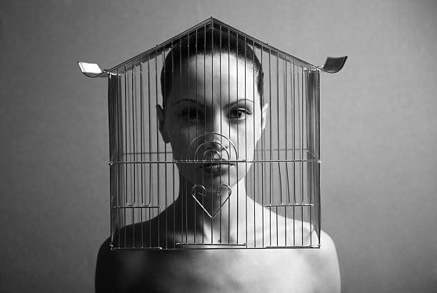 Black and white surreal image stern naked woman in birdcage stock photo