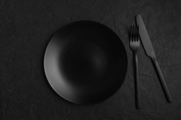Black background with plate and cutlery, monochrome table setting Black background with plate and cutlery, monochrome table setting matte finish stock pictures, royalty-free photos & images