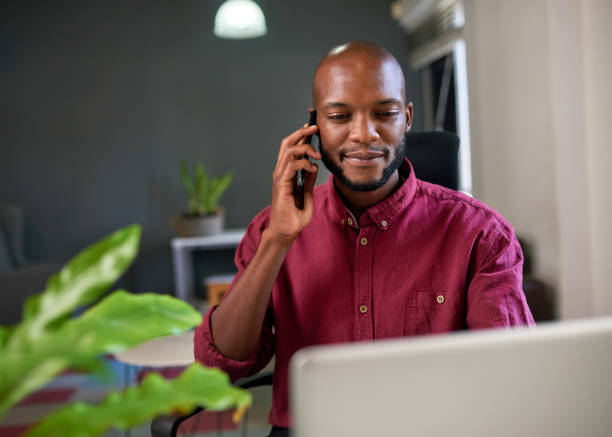 A Black businessman looks at his screen while answering call in the office stock photo