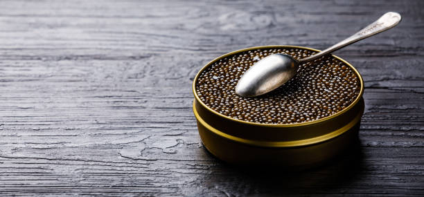 Black caviar in can and silver spoon Black caviar in can and silver spoon on black wooden background copy space roe stock pictures, royalty-free photos & images