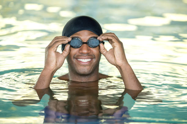 Black cheerful young man putting on the swimming goggles looking at camera very happy at the pool Black cheerful young man putting on the swimming goggles looking at camera smiling very happy at the pool swimming goggles stock pictures, royalty-free photos & images