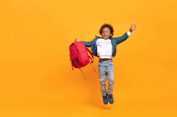 Black child boy 3 years, Students kid jumping to happy enjoy come back to school with red school bag, Isolated portrait on yellow background with copy space, International student happiness stock photo
