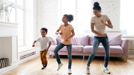 Active leisure together with kids. Millennial african mother teaching school age daugter and little son modern dance movements, black boy and girl spend time at dancing with young babysitter at home