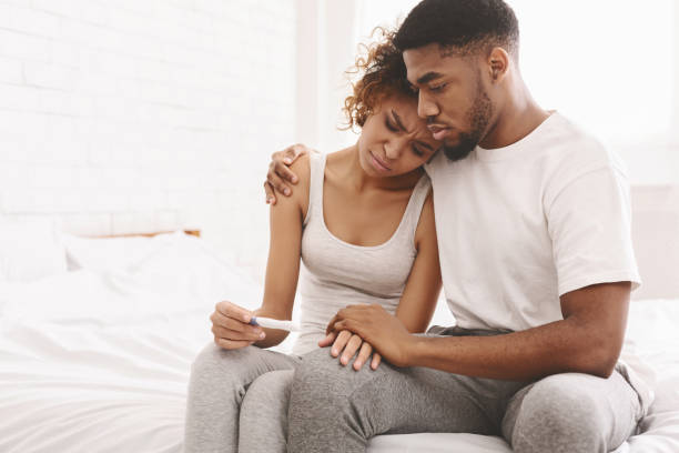 Black couple with a negative pregnancy test result Infertility problem. Upset african american couple sitting on bed with negative pregnancy test result, free space fertility stock pictures, royalty-free photos & images