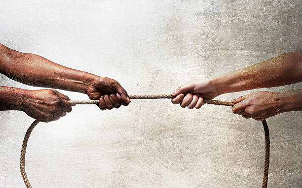 black ethnicity hands pulling rope against white Caucasian race person stock photo