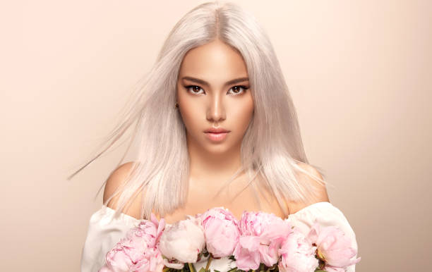 Black eyed beautiful blonde woman with oriental appearance is holding bouquet of rose peonies.Hairdressing and professional dyeing. stock photo