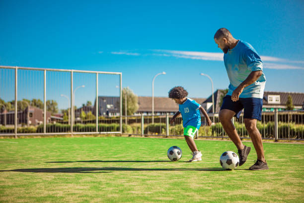 Black father and young son training on the football pitch stock photo