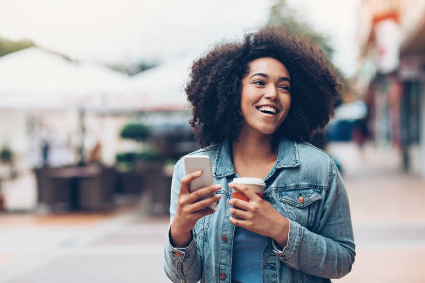 zwarte meid met telefoon en koffie outdoors in de stad - walking with coffee stockfoto's en -beelden