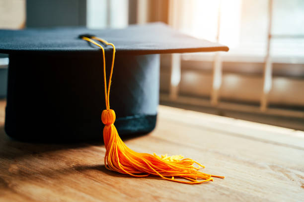 black graduation cap and yellow tassel place on wooden table stock photo