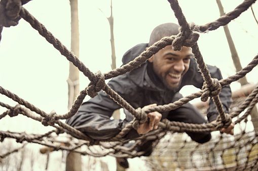 Black handsome young man climbing over obstacle during mud run