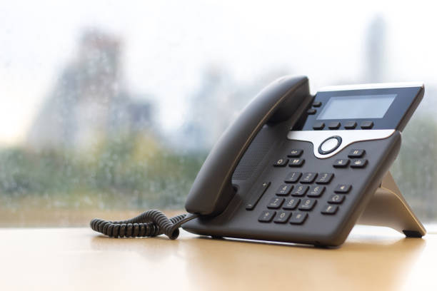 Black IP Phone on wooden table , Telephone on desk with big window city view.Modern office concept. Black IP Phone on wooden table , Telephone on desk with big window city view.Modern office concept. voip stock pictures, royalty-free photos & images