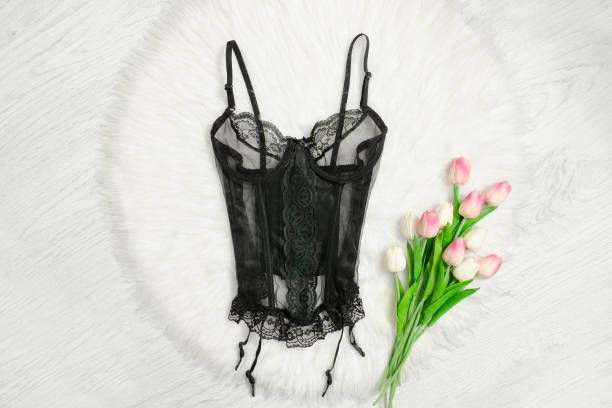 Black lace corset on white fur. Pink tulips. Fashionable concept. Black lace corset on white fur. Pink tulips. Fashionable concept. bodice stock pictures, royalty-free photos & images