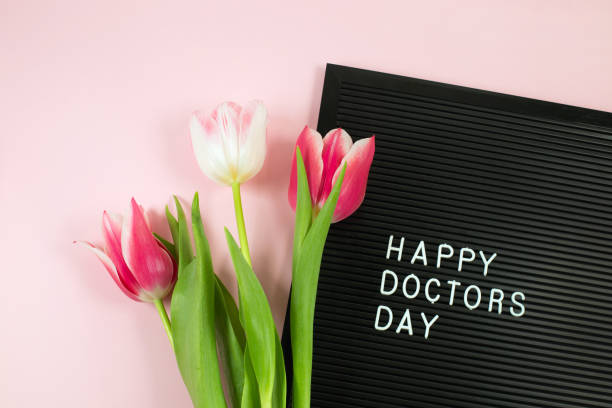 Black letterboard with white plastic letters with quote Happy Doctor's day and Bunch of pink tulips on pink background. stock photo