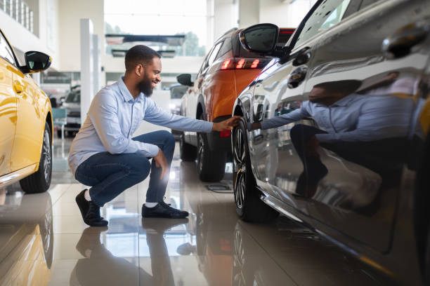 black male customer choosing new automobile in dealership center, examining wheel rims - köpa däck bildbanksfoton och bilder