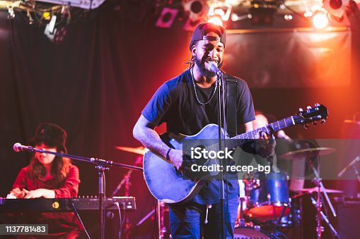 istock Black male guitarist singing and playing acoustic guitar on stage 1137781483