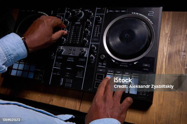 Black man DJ uses control desk to create song.