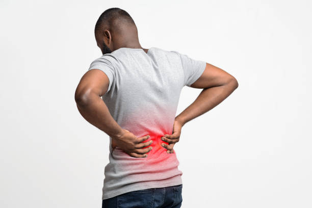 Black man holding his hands on lower back Afro guy holding both hands on lower back, pain in spine, inflamed zone highlighted in red, white background, free space back pain stock pictures, royalty-free photos & images