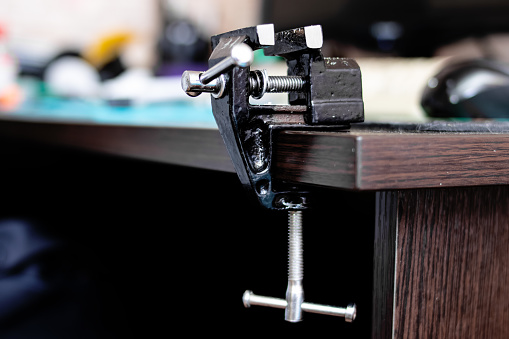 Black metal vise on the edge of a wooden table close up