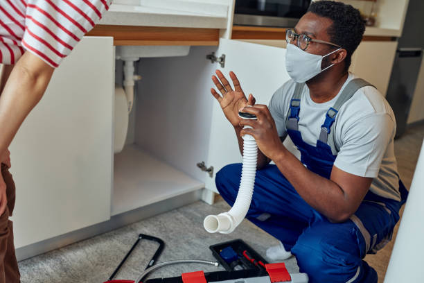 Black plumber with customer in her kitchen Black handyman in overalls installing a kitchen sink on an customer’s home. He is wearing protective face mask african american plumber stock pictures, royalty-free photos & images