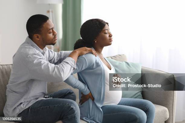 Black pregnant woman suffering from back pain at home