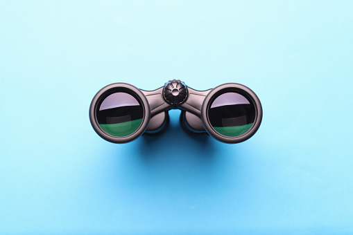 Black professional binoculars lying on blue background. Page not found error 404 concept
