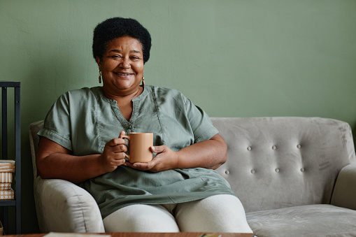 Portrait of black senior woman smiling at camera while enjoying cup of coffee at home, copy space