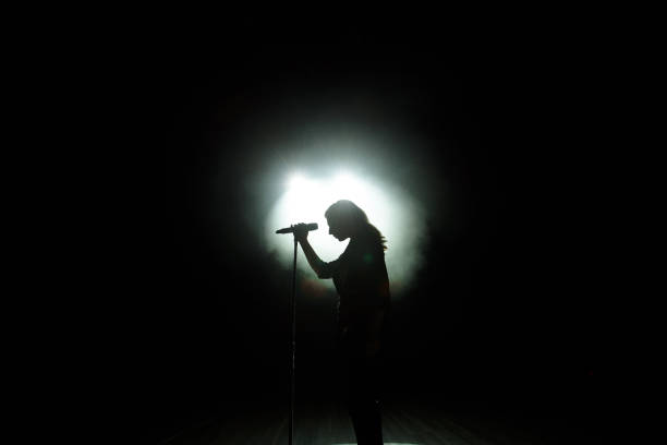 black silhouette of female singer with white spotlights in the background stock photo