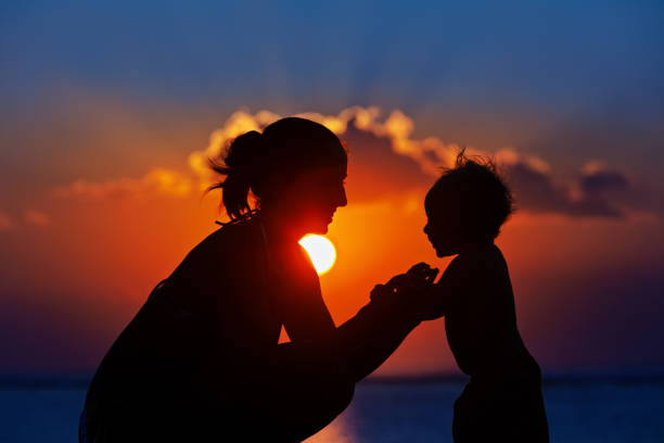 Black silhouette of mother, baby son walk by sea beach stock photo