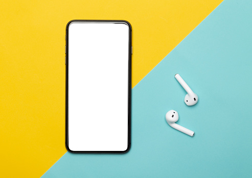 Black smartphone with blank screen and wireless earphones isolated on yellow and blue background. Clipping path.