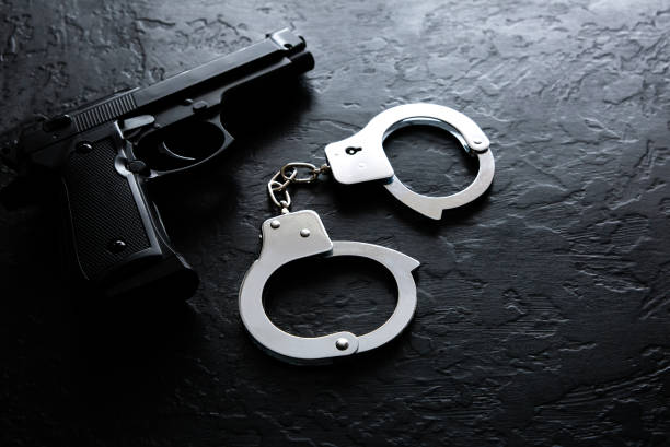 Black steel gun and Police metal real handcuffs lie on the black background. Private detective work. Searching information. Crime and robbery, prison concept. Black steel gun and Police metal real handcuffs lie on the black background. Private detective work. Searching information. Crime and robbery, prison concept. gun violence stock pictures, royalty-free photos & images