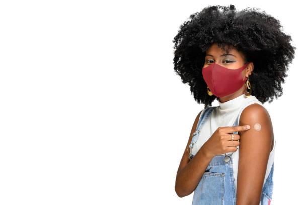 schwarzer teenager trägt schutzmaske gegen covid-19 mit einem lächeln auf dem gesicht zeigt die impfstoffmarke, isoliert auf weißem hintergrund - impfen stock-fotos und bilder