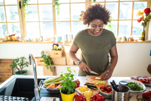 black woman cutting vegetables in kitchen - woman chopping vegetables imagens e fotografias de stock