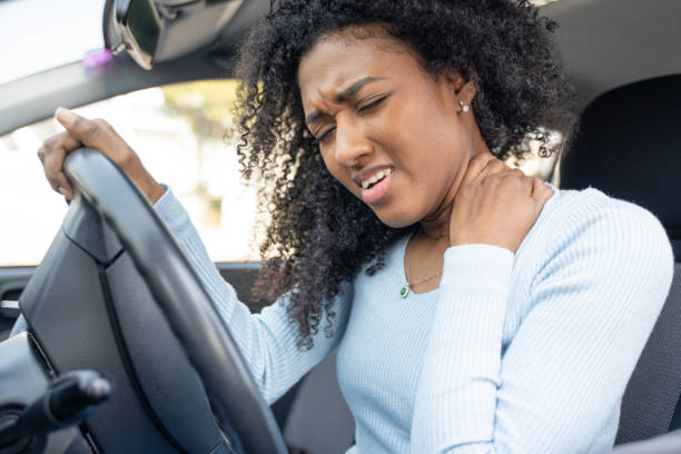 a black woman hurts her neck after a car accident - fixing car pain stockfoto's en -beelden