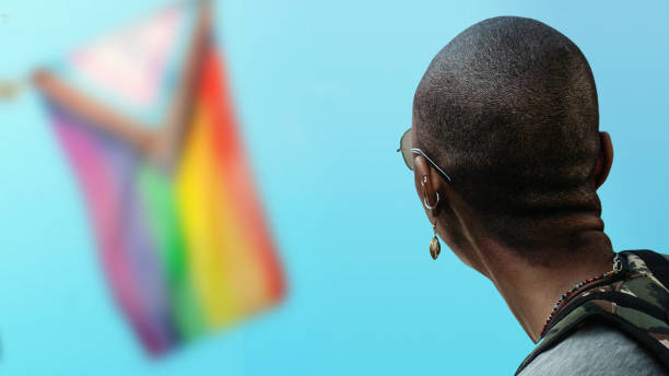 чернокожая женщина смотрит на флаг progress pride во время парада гордости. - progress pride flag стоковые фото и изображения