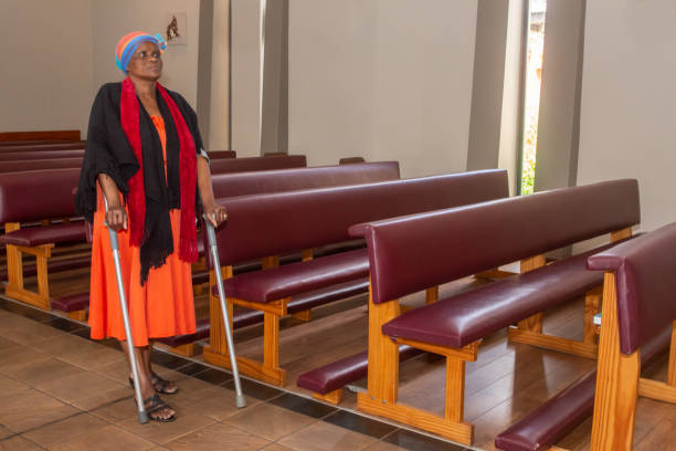 Black woman on crutches walking along church aisle. stock photo