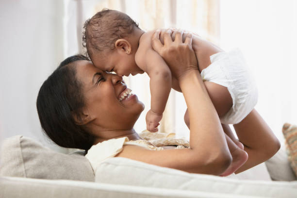 Black woman playing with baby daughter on sofa stock photo
