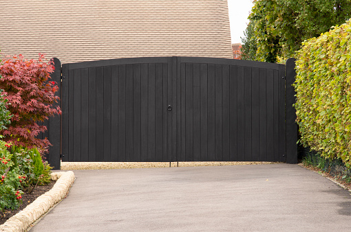 A black, wooden gate bars entry from hedge lined driveway