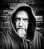 A mature, bearded man in a hoodie looks at camera, frowning, in this moody black-and-white portrait.