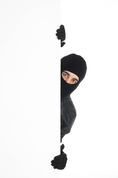 Black-wearing thief spying out the white wall/background stock photo