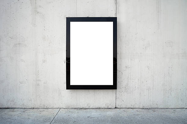 Blank billboard on wall. Blank billboard on wall. Wall is made of concrete and gray coloured. Billboard is oriented vertically and standing on the middle of frame. Edges of billboard are black. Billboard is empty so you can write or add something on it. - Clipping path of billboards included. billboard posting stock pictures, royalty-free photos & images