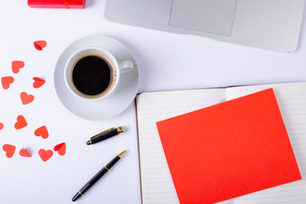 Blank red paper on open diary with copy space by coffee and heart shape at desk stock photo