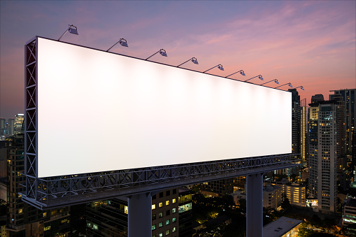 Blank white road billboard with Bangkok cityscape background at night time. Street advertising poster, mock up. Side view. The concept of marketing communication to sell idea.