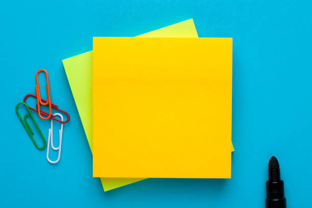 Blank yellow note for add text message Yellow note with empty place for your text with marker and paper clips on blue background. Reminder concept. Post-It notes stock pictures, royalty-free photos & images