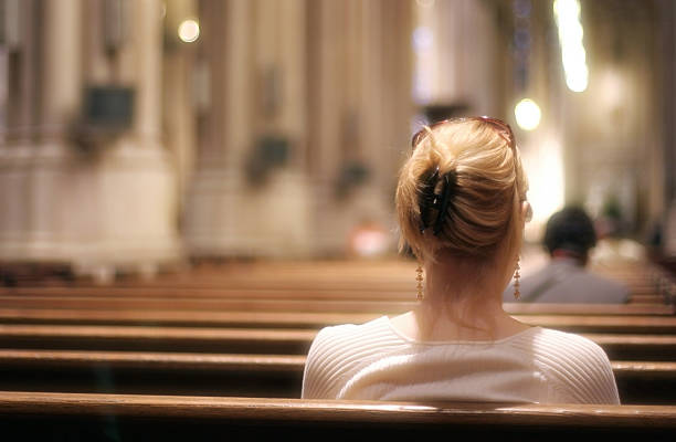 Blonde woman sitting on a church bench praying stock photo