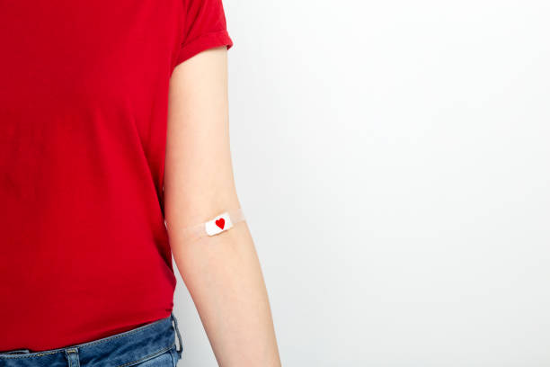 Blood donorship. Young girl in red T-shirt hand taped with patch with red heart after giving blood on gray background. Copy space Blood donorship. Young girl in red T-shirt hand taped with patch with red heart after giving blood on gray background. Copy space blood photos stock pictures, royalty-free photos & images
