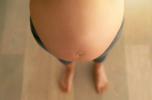 Cropped high angle shot of a pregnant woman’s bare belly