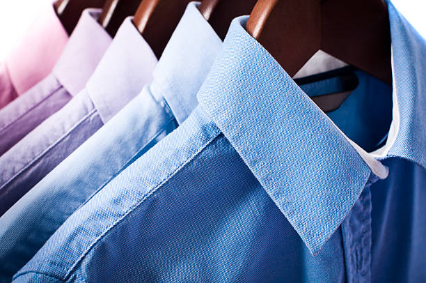 blue and pink elegant button down shirts hanging on hangers - stomerij stockfoto's en -beelden